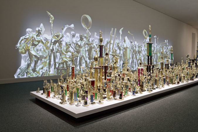 Jean Shin, Everyday Monuments, 2009 Sports trophies, painted cast and sculpted resins, projections Floor Installation: Dimensions variable, approximately 7.33 ft h x 5 ft w x 45 ft d Wall Projection: 9.33 ft h x 42 ft w Commissioned by the Smithsonian American Art Museum, Washington, D.C.